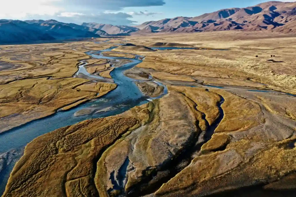 Imagem aérea de um rio serpenteando através de uma paisagem desértica com montanhas ao fundo, ilustrando a identificação de aquíferos profundos usando som e campos elétricos.