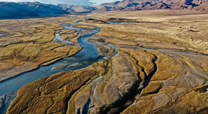 Imagem aérea de um rio serpenteando através de uma paisagem desértica com montanhas ao fundo, ilustrando a identificação de aquíferos profundos usando som e campos elétricos.