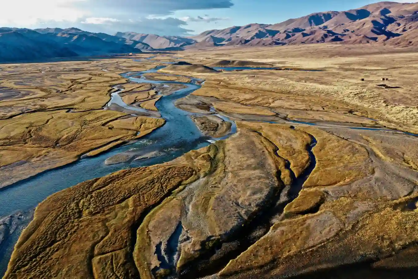 Imagem aérea de um rio serpenteando através de uma paisagem desértica com montanhas ao fundo, ilustrando a identificação de aquíferos profundos usando som e campos elétricos.