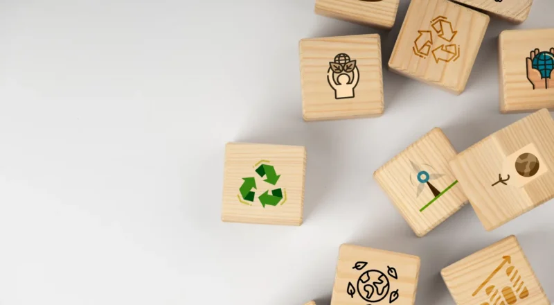 Blocos de madeira com ícones de reciclagem e sustentabilidade sobre fundo branco, simbolizando Economia Circular na Indústria: Reaproveitamento de Resíduos Como Vantagem Competitiva e práticas de reutilização