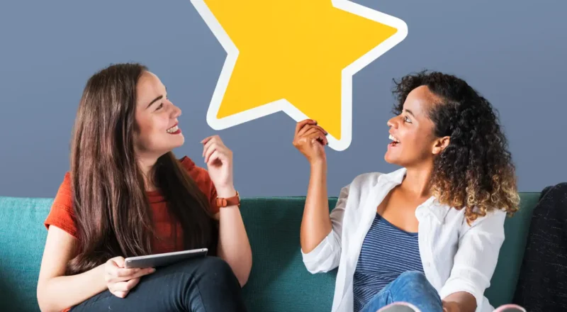 Duas mulheres sorridentes trocando uma estrela dourada em um ambiente informal, simbolizando a influência do marketing de experiência na mudança do comportamento de compra.