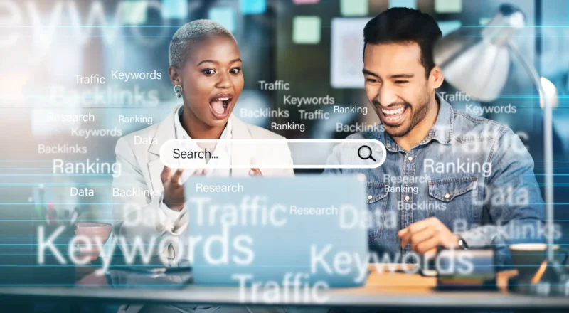 Imagem de marketing digital com duas pessoas em frente ao computador, interface com barra de busca e elementos visuais de SEO como palavras-chave, ranking, backlinks e traffic.