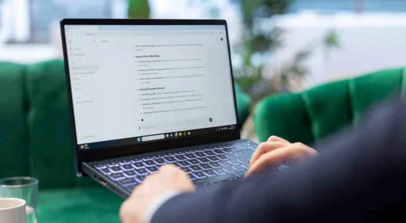 Como Monitorar a Menção da Sua Marca Em ChatGPT, Gemini e Perplexity: Pessoa usando notebook em um ambiente de escritório, digitando enquanto visualiza um documento na tela, com foco na leitura e no monitoramento de informações.